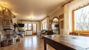 Een ruime woonkamer met een stenen open haard, een grote houten tafel en een gezellige zithoek.