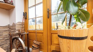 Een rustiek interieur met een houten deur, een groot raam, een stenen muur, een houten vat en een plant in een pot.