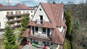 A two-story house with a sloped roof, a balcony on the upper floor, and a small deck area with outdoor furniture. - Mountain Spirit Dream Studio (Zakopane)