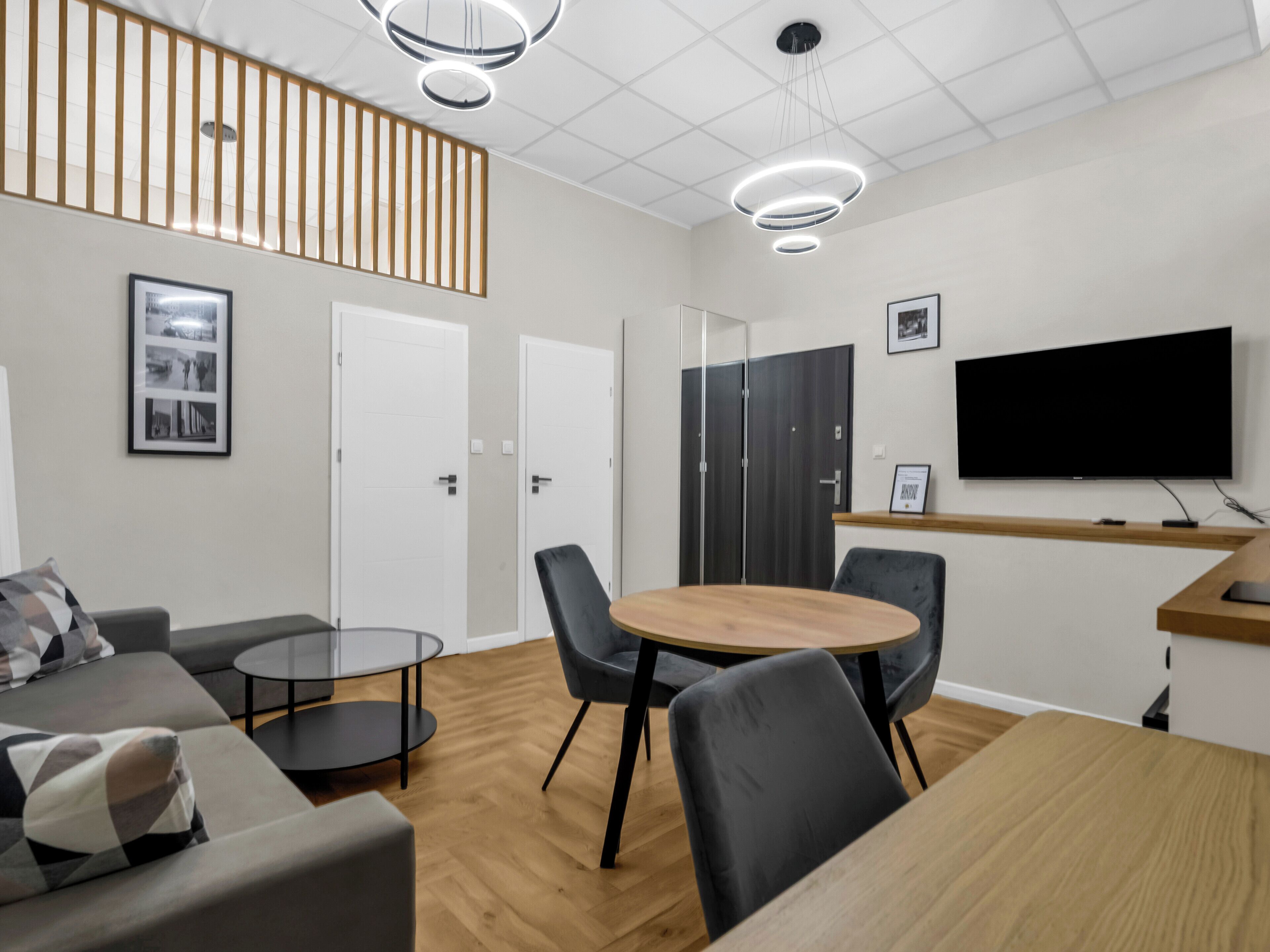 Une salle de réunion moderne équipée d’une table ronde, de deux chaises, d’un canapé et d’un téléviseur fixé au mur.