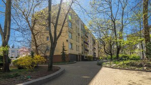 A paved pathway leading to a multi-story residential building with balconies, surrounded by trees and greenery.
