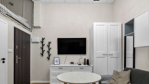 A modern living room with a flat-screen TV, a white cabinet, a grey sofa, and a round wooden table.