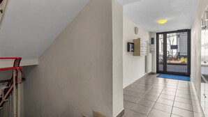 A clean, modern hallway with a staircase, a door leading outside, and a blue mat at the entrance.