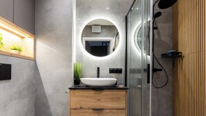 Une salle de bain moderne avec un meuble-lavabo en bois, un lavabo blanc et une cabine de douche en verre.
