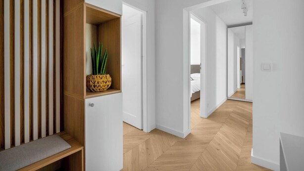 A modern hallway with wooden flooring, white walls, and a built-in shelf with a plant. - Warszawa Rakowiec Stylish Apartment (Warszawa)