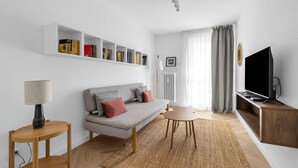 A modern living room with a grey sofa, a TV on a wooden stand, a bookshelf, and a lamp. - Warszawa Rakowiec Stylish Apartment (Warszawa)