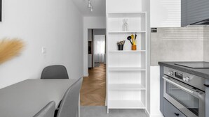 A modern kitchen with white cabinetry, a built-in oven, and a dining area with a gray chair. - Warszawa Rakowiec Stylish Apartment (Warszawa)
