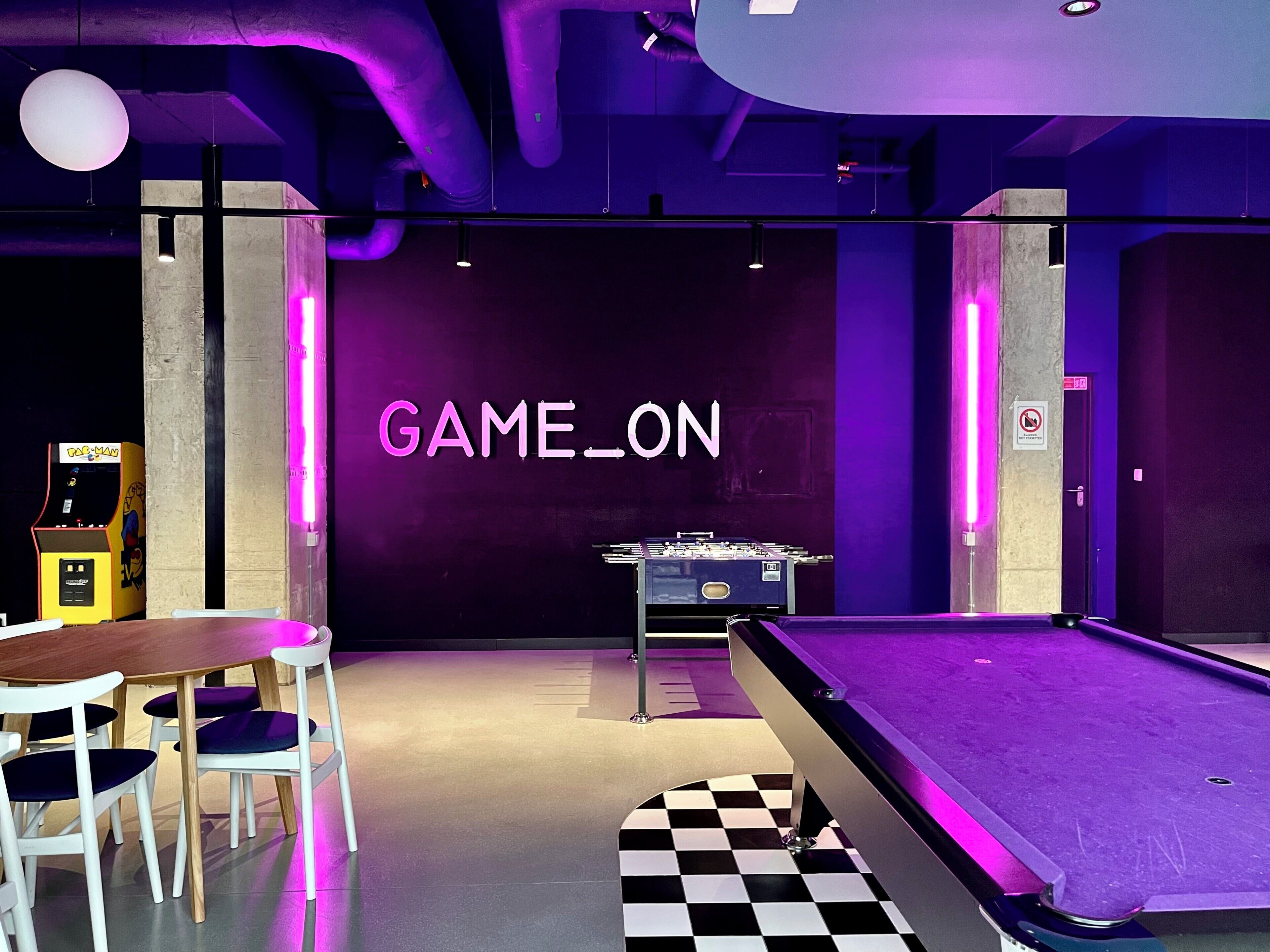 A room with a pool table, a foosball table, and a neon sign reading "GAME_ON".