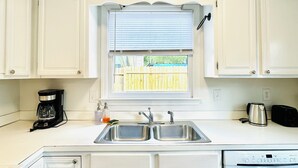 A kitchen with white cabinets, a double sink, a coffee maker, a toaster, and a dishwasher. - Cozy and Charming House (Pineville)