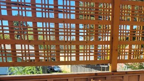 A wooden deck with a table and two chairs, a wooden fence, and a view of a residential area. - The Nest in South Eugene (Eugene)