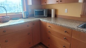 A kitchen with wooden cabinets, a microwave, a kettle, and a window with a view of trees. - The Nest in South Eugene (Eugene)