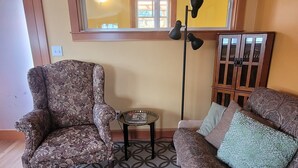 A living room with a patterned rug, a floral armchair, a sofa with patterned cushions, a floor lamp, and a window with a view. - The Nest in South Eugene (Eugene)