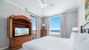 Habitación de hotel con una cama grande, un aparador de madera con un televisor, una silla y vistas al océano.