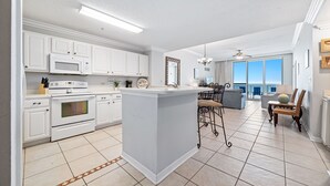 Cocina moderna con armarios blancos, una isla central y un comedor con vistas.
