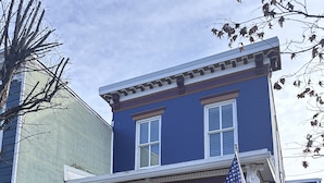 A two-story house with a porch, a flag, and a security sign.