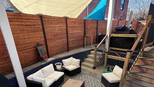 An outdoor patio area with a wooden deck, a covered seating area with cushions, and a staircase leading to an upper level.