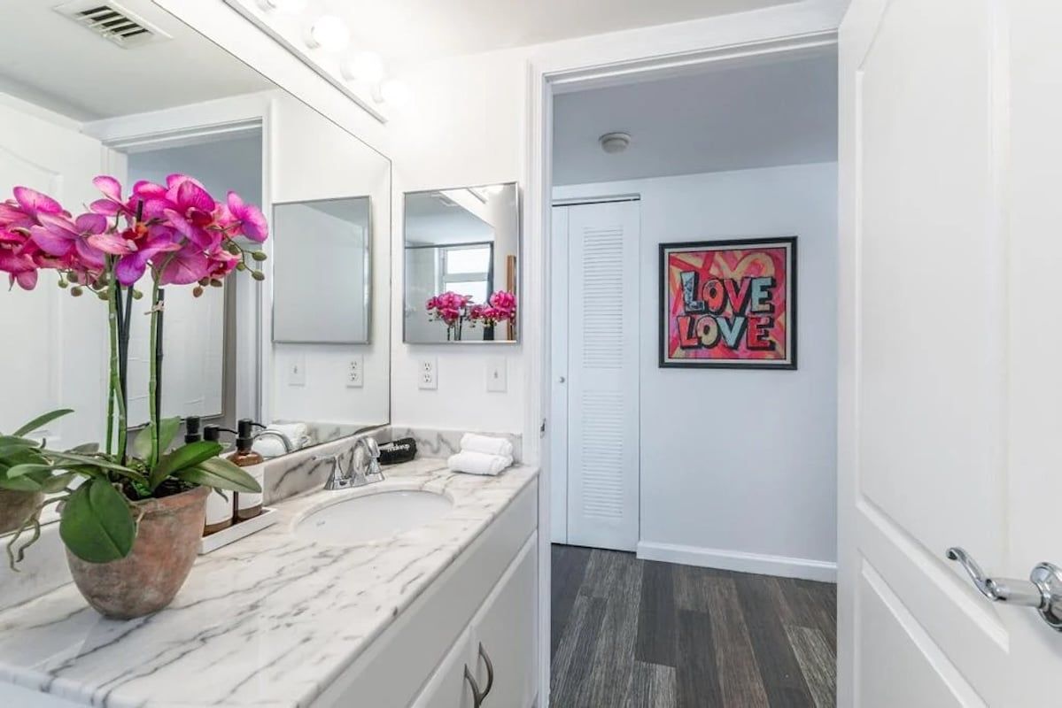 A modern bathroom with a marble sink, a large mirror, and a 'LOVE LOVE' poster on the wall.