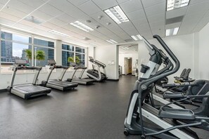 Ein Fitnessstudio mit Laufbändern, Ergometer und einem großen Fenster mit Blick auf die Stadt.