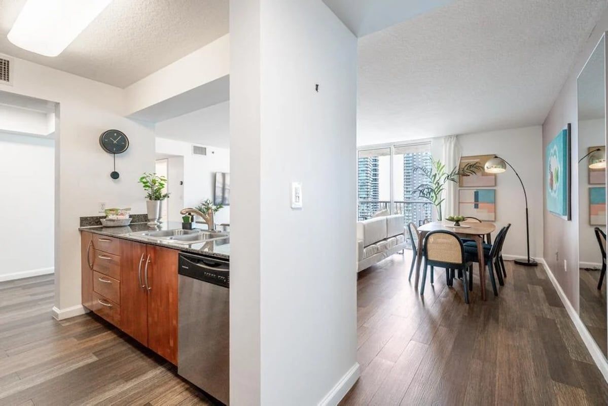 A modern kitchen with a dishwasher, wooden cabinets, and a clock on the wall.