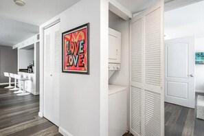 Un couloir avec une porte blanche, une œuvre d’art encadrée et un espace dédié à la buanderie.