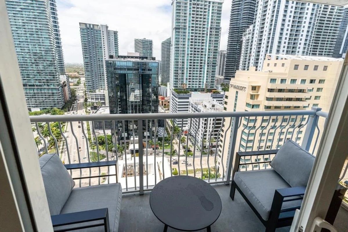 A balcony with two chairs and a small table, overlooking a cityscape with high-rise buildings.