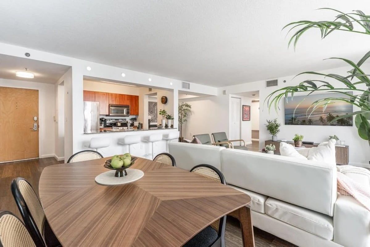Una sala de estar moderna con una mesa de comedor, un sofá blanco y una cocina al fondo.