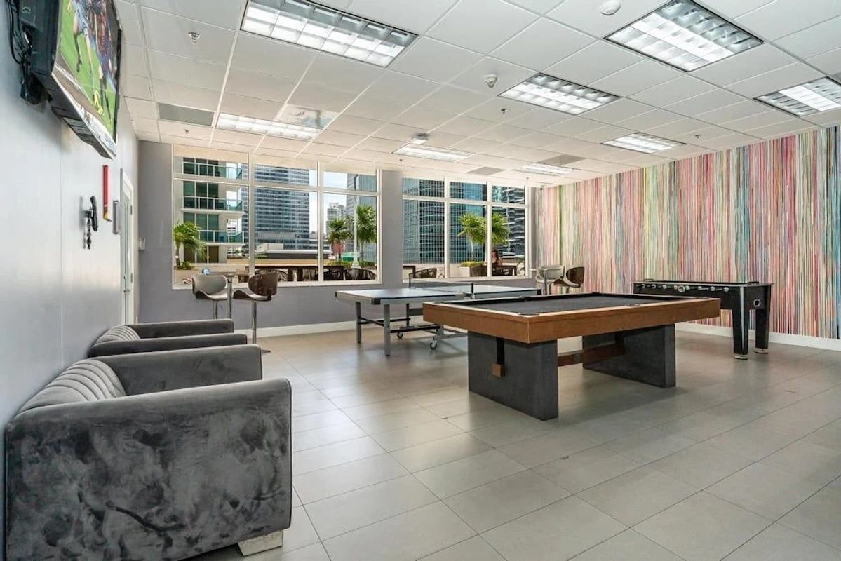 A modern indoor recreational area with a pool table, seating, and large windows offering city views.