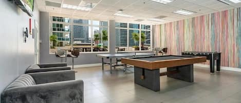 A modern indoor recreational area with a pool table, seating, and large windows offering city views.