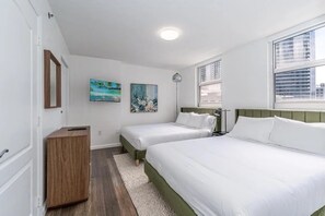Une chambre avec deux lits, une table de chevet, une lampe, un tableau et une fenêtre avec des stores.