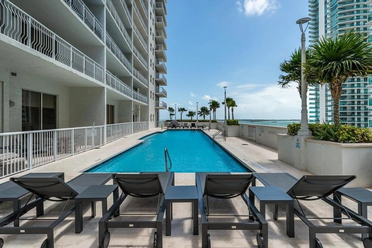 A rooftop pool with lounge chairs, a view of the ocean, and a high-rise building with balconies.