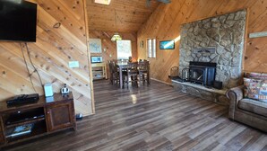 Un intérieur de chalet chaleureux avec une cheminée en pierre, des murs en bois, un coin repas et un téléviseur.