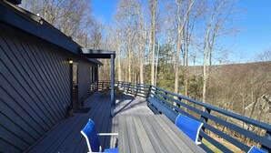 Une terrasse en bois avec des chaises bleues et une balustrade, donnant sur une zone boisée.