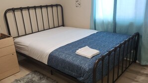 A single bed with a metal frame, a white mattress, a blue blanket, and a folded white towel. There is a wooden dresser to the left and a grey furry rug on the floor. - 3 bedroom, 2 bathroom across from Walmart, 5 minutes to the airport & hospital. (Yellowknife)
