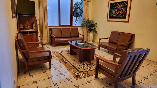 Uma sala de estar com sofá, poltronas, mesa de centro, televisão e uma janela grande com cortinas.