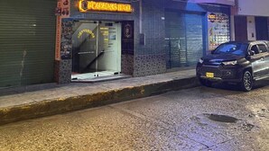 Um hotel com um letreiro de neon, uma loja fechada com um aviso que diz "Cafeteria's Hotel", e um carro estacionado na rua.