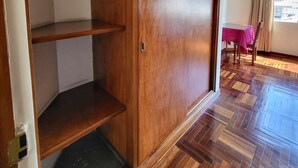Quarto com guarda-roupa de madeira, uma mesa com toalha vermelha e janela com cortinas.