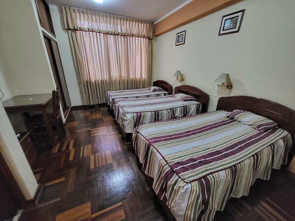A hotel room with three beds, wooden flooring, a window with curtains, and two wall-mounted lamps. - D CARDENAS HOTEL (Cajamarca)