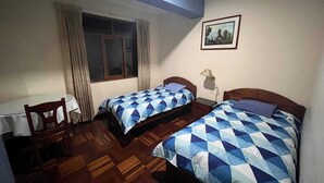 Quarto com duas camas, uma escrivaninha e uma janela com cortinas.