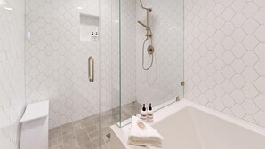 A modern bathroom with a glass-enclosed shower, a white bathtub, and a hexagonal tile pattern on the walls.