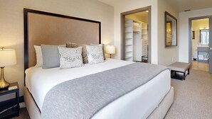 A hotel room with a large bed, bedside lamps, a bench, and a walk-in closet.