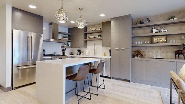 A modern kitchen with a central island, bar stools, stainless steel appliances, and decorative items on shelves.