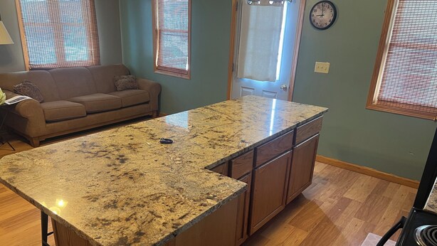 A kitchen with a granite countertop, wooden cabinets, a built-in oven, and a dining area with a couch. - The Bohemian Bungalow  near Main Street in Scenic Verdigre, Nebraska (Verdigre)