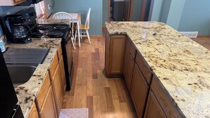 A kitchen with wooden cabinets, a granite countertop, a coffee maker, and a dining area with chairs. - The Bohemian Bungalow  near Main Street in Scenic Verdigre, Nebraska (Verdigre)