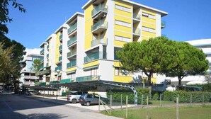 A multi-story residential building with balconies, a covered parking area, and a tree in front.