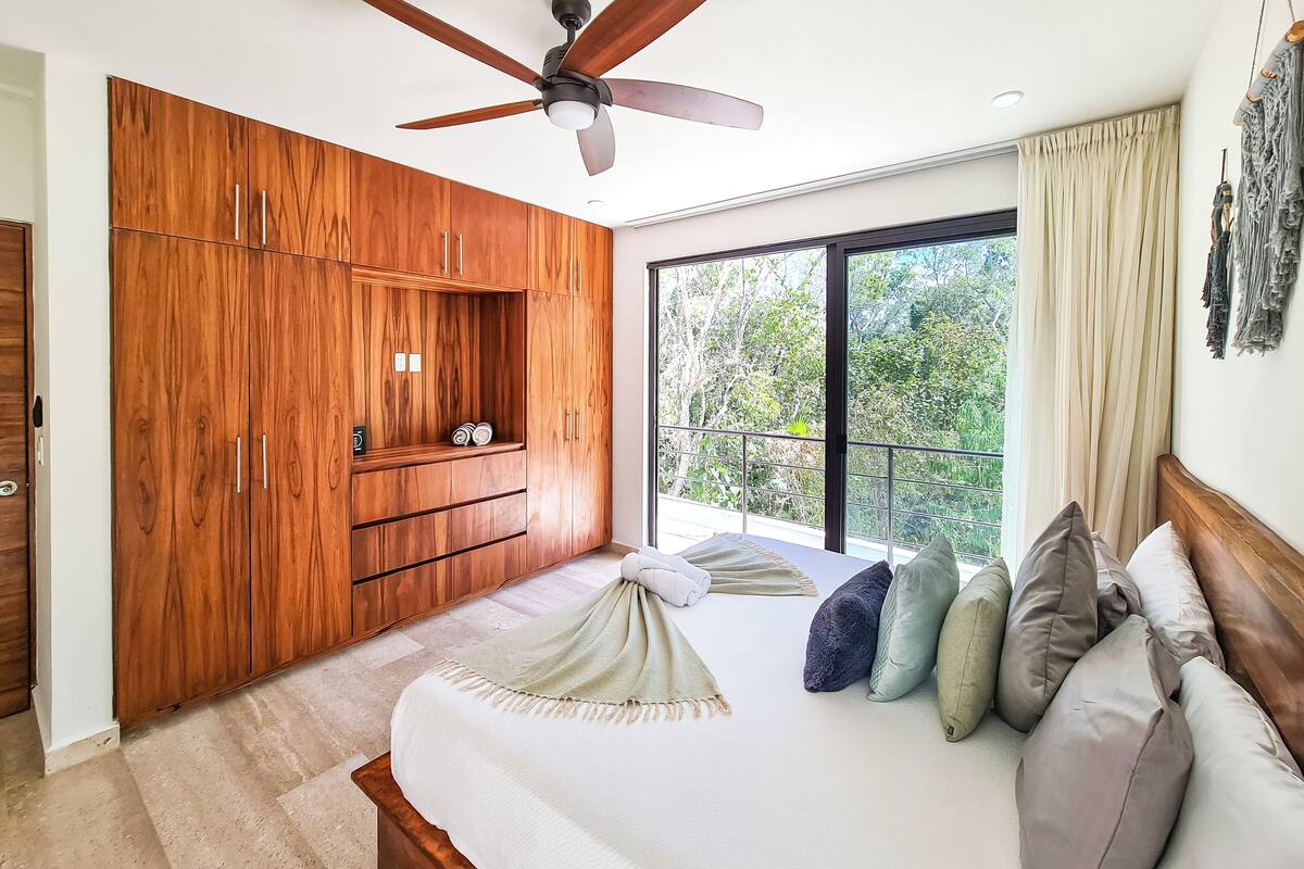 Ein Schlafzimmer mit einem großen Bett, einem Holzschrank, einem Deckenventilator und Blick ins Grüne durch das Fenster.
