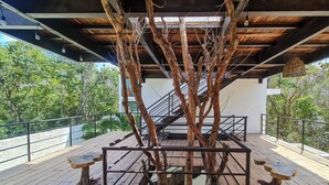 Un pont de fusta amb un tronc d'arbre al centre, envoltat de baranes metàl·liques i bancs.