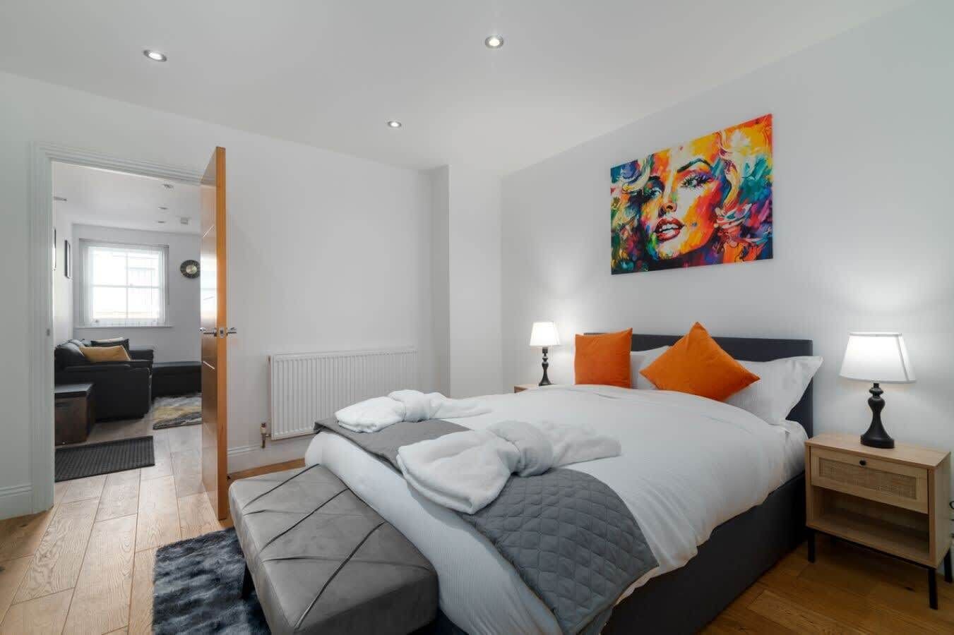 A modern bedroom with a large bed, two bedside lamps, and a vibrant abstract painting on the wall.