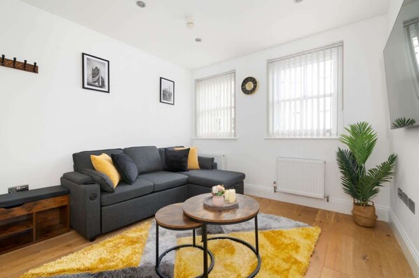 Una sala moderna con un sofá modular, una mesa de centro y un ventanal con persianas.