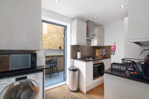 A compact kitchen with a microwave, washing machine, and a coffee station.