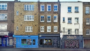 A row of multi-story buildings with various storefronts, including a sushi shop and a tattoo parlor. - Stylish Brick Lane Apartment with Balcony Sleeps 4 (Greater London)